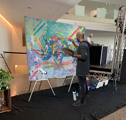 Der Künstler steht vor einer Leinwand und malt ein Nashorn in knalligen Farben.