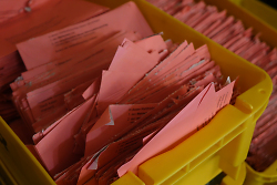 Auf dem Bild sind rosafarbene Stimmzettel für die Wahlen in gelben Boxen zu sehen.
