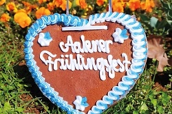 Auf dem Bild ist ein Lebkuchenherz mit der Aufschrift Aalener Frühli8ngsfest zu sehen. Im Hintergrund ist eine Blumenwiese.