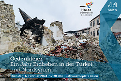 Das Bild zeigt Häuserruinen in Antakya, davor ein Schriftzug mit dem Datum der Gedenkfeier anlässlich des Erdbebens.
