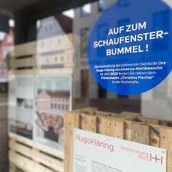 Auf dem Bild ist ein Schaufenster mit einem Aufkleber zu sehen, der auf die Ausstellung des Hugo-Häring-Preises hinweist.