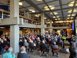 Auf dem Bild sind viele Menschen im Foyer des Aalener Rathaus zu sehen, die einem Vortrag zuhören.