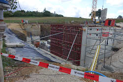 Das Bild zeigt eine Baustelle des Überlaufbeckens. Zwei Wände sind bereits betoniert, ein Baukran steht daneben.