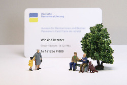 Auf diesem Bild ist ein Ausweis der Deutschen Rentenversicherung zu sehen sowie kleine Spielzeugfiguren alter Menschen, die am Stock gehen oder gemeinsam auf einer Bank sitzen.