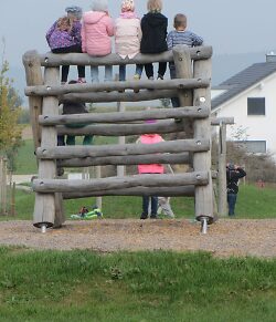 Auf dem Bild ist ein Klettergerüst auf dem Spielplatz Schießmauer zu sehen, auf dem vier Kinder sitzen.