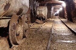 Auf dem Bild ist ein alter Bergbauwaggon zu sehen. Daneben liegt ein Tunnel mit Schienen.
