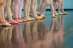 Auf dem Bild sind die Beine von jungen Balletttänzer*innen zu sehen.