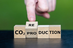 Auf dem Bild ist eine Hand zu sehen, die das Wort CO2-Production abgebildet durch Buchstabensteinchen in CO2-Reduction abwandelt.