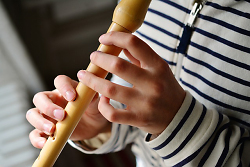Auf dem Bild ist ein Kind zu sehen, das auf einer Blockflöte musiziert.