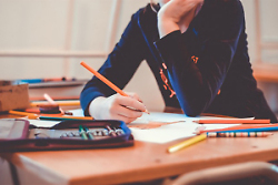 Auf dem Bild ist ein Schulkind zu sehen, das an einem Tisch sitzt und einen Stift in der Hand hält.